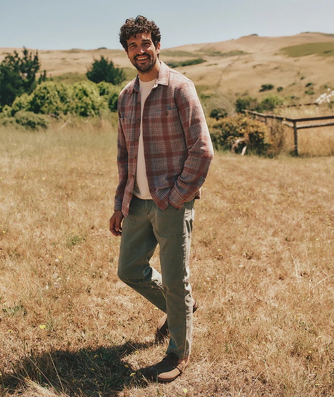 Model weraing Marine Layer Breyer Relaxed fit utility pant in vetiver (Green) color, front  view in a stylized shot with vegetation in the background