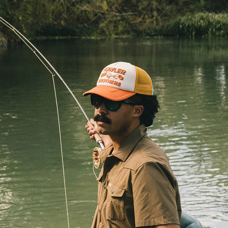 Lifestyle photo of a man fishing, wearing Howler Bros. Foam Front Trucker hat with lone Gull logo on front, front view